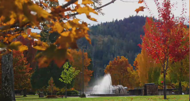A scenic park in autumn, featuring colorful trees and a fountain, with a backdrop of mountains.